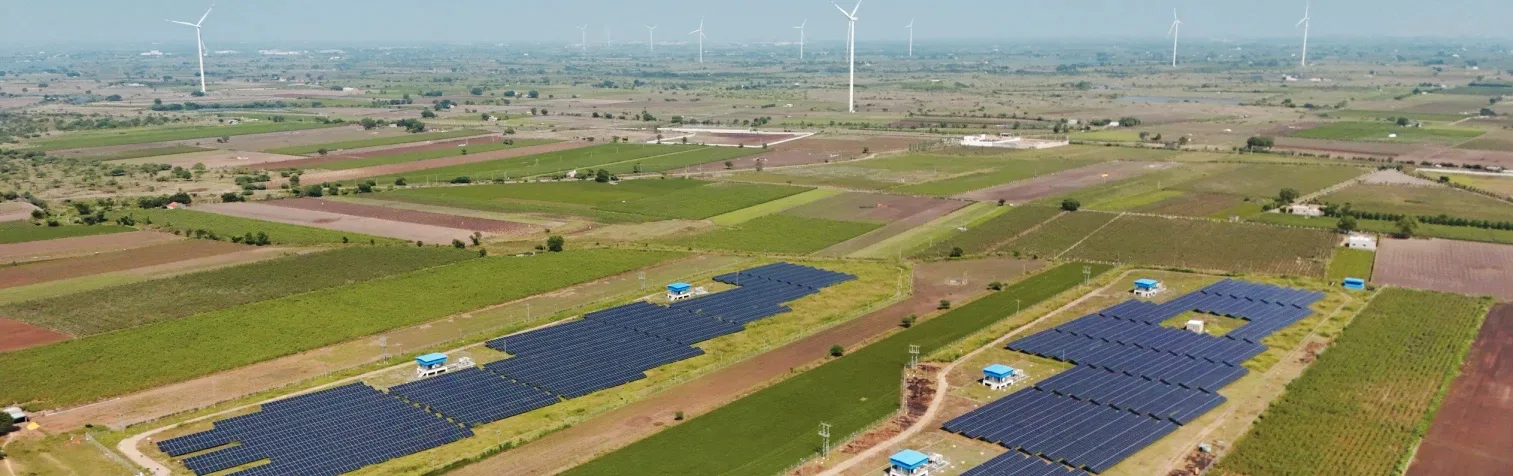 Aerial view of the Laxcon Steels wind solar hybrid site, turbines on the horizon above rows of solar arrays